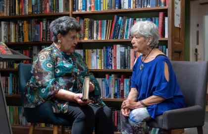 Two people sat facing each other talking in front of bookshelves in Hove Library