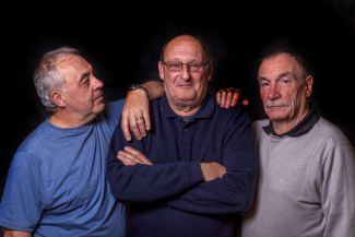 Photo of three men stood close together to depict peer support