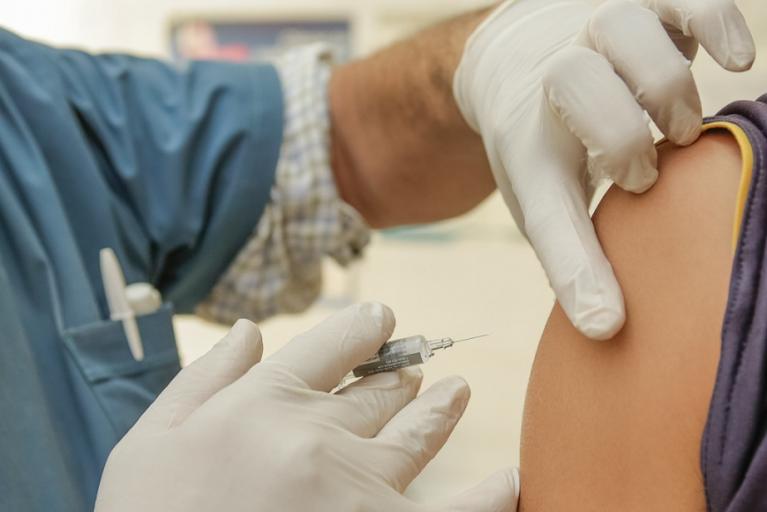 Image depicting needle and vaccination being administered into upper arm