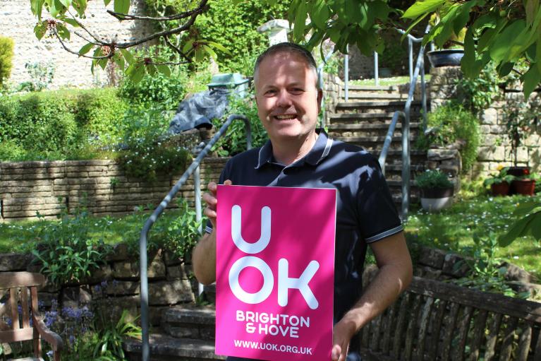 Photo of UOK Team member stood holding board showing new bright pink UOK logo and web address