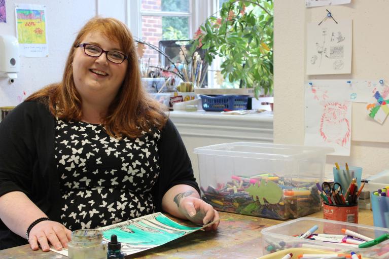 Photo of client in art room sat at desk with artwork, smiling